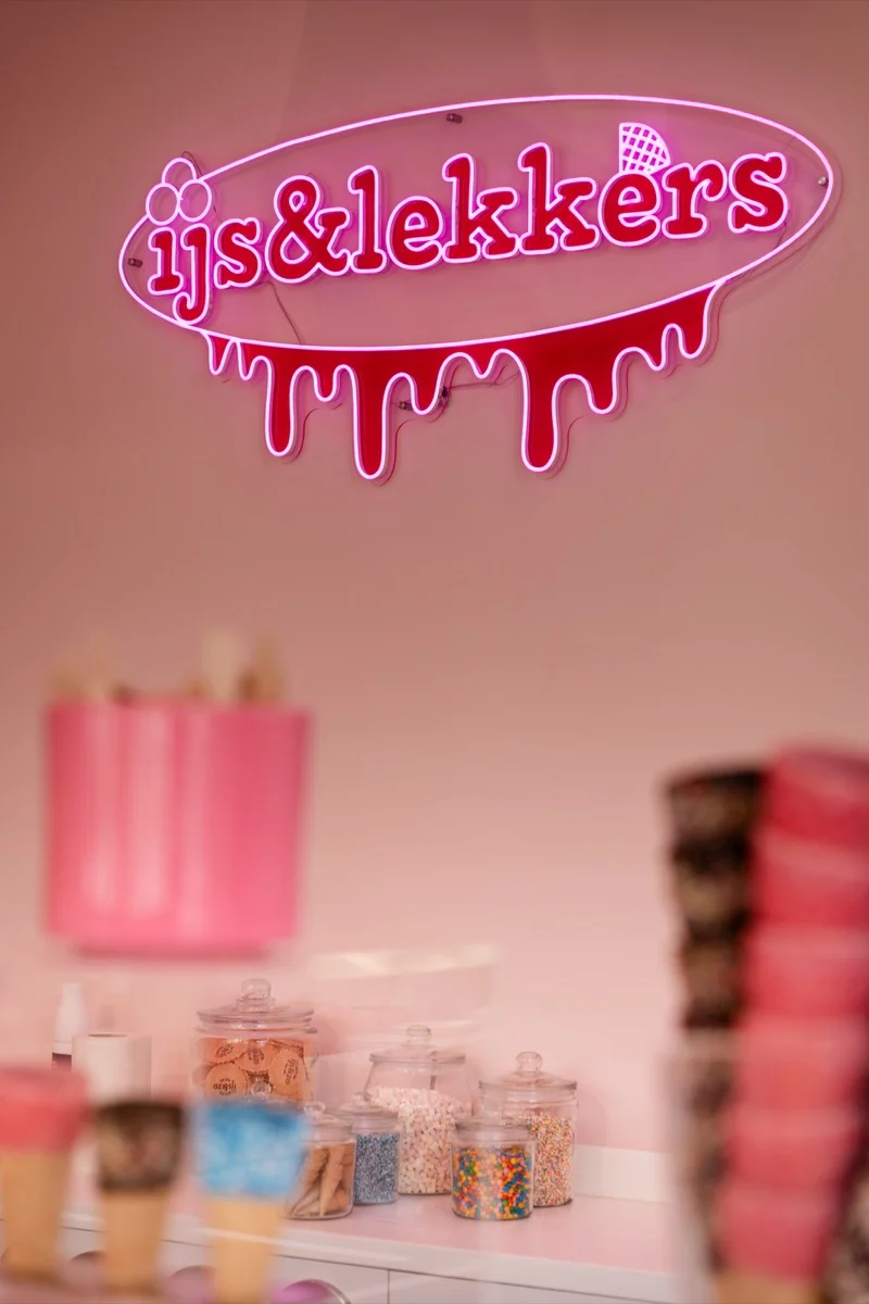 Neonbord ijs&lekkers boven de toonbank met decoratieve potten en gedecoreerde ijshoorntjes