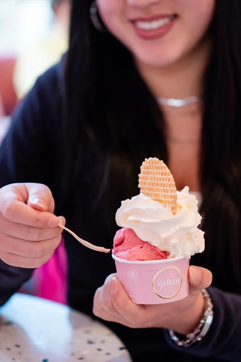 Handen houden een roze ijsbeker met slagroom en wafelhart bij IJs & Lekkers